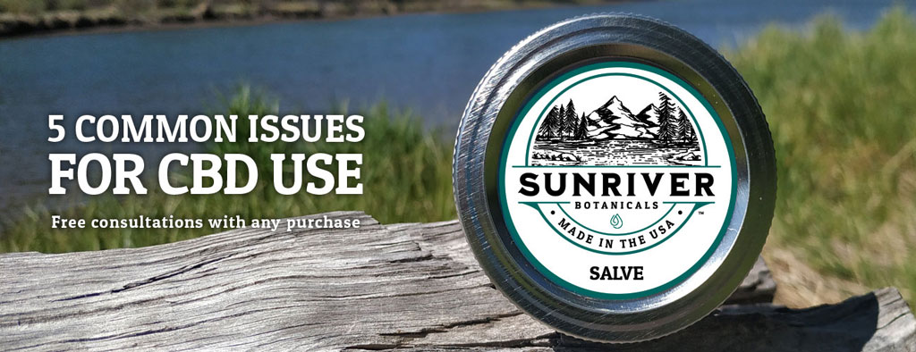 Close up of Sunriver Botanicals CBD salve lid. Lid with a white label resting on a log with grass & water in the background.